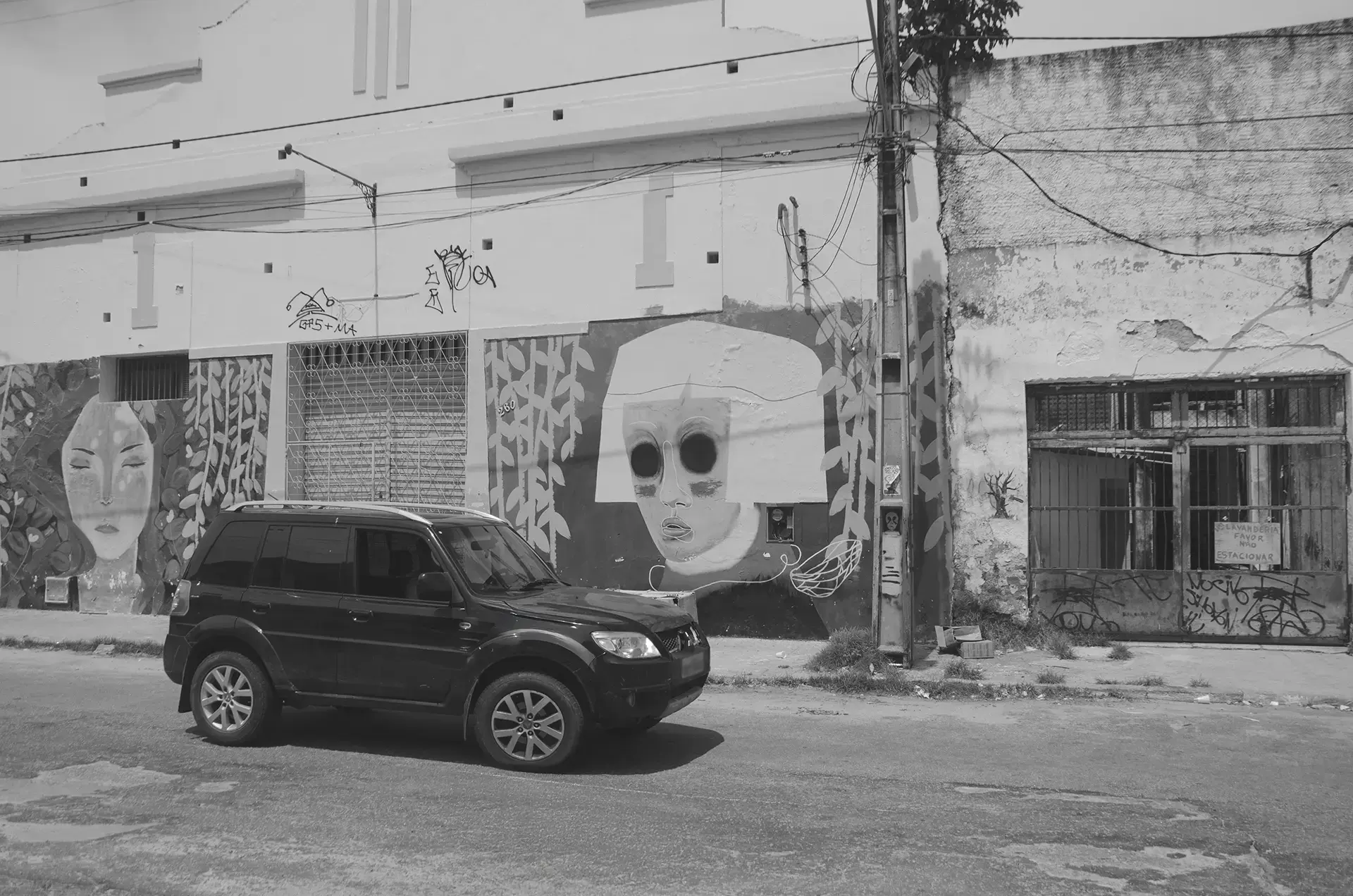 Frame 1 em tons de cinza de uma sequencia que mostra um carro atravessando uma rua no Centro de Fortaleza da esquerda para a direita com um mural de graffiti ao fundo