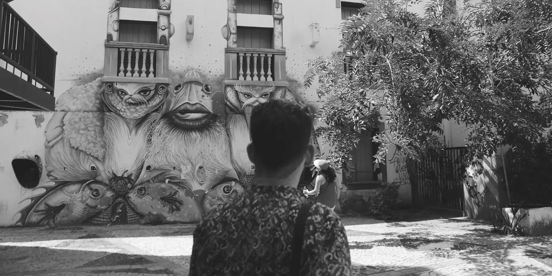 Fotografia em tons de cinza de um homem de costas olhando para um mural de graffiti no Centro Cultural Dragão do Mar de Arte e Cultura