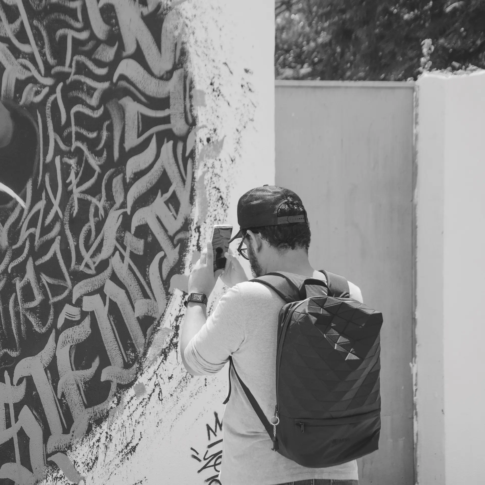 Fotografia em tons de cinza de pessoas fazendo fotos com o celular em frente a um mural de graffiti