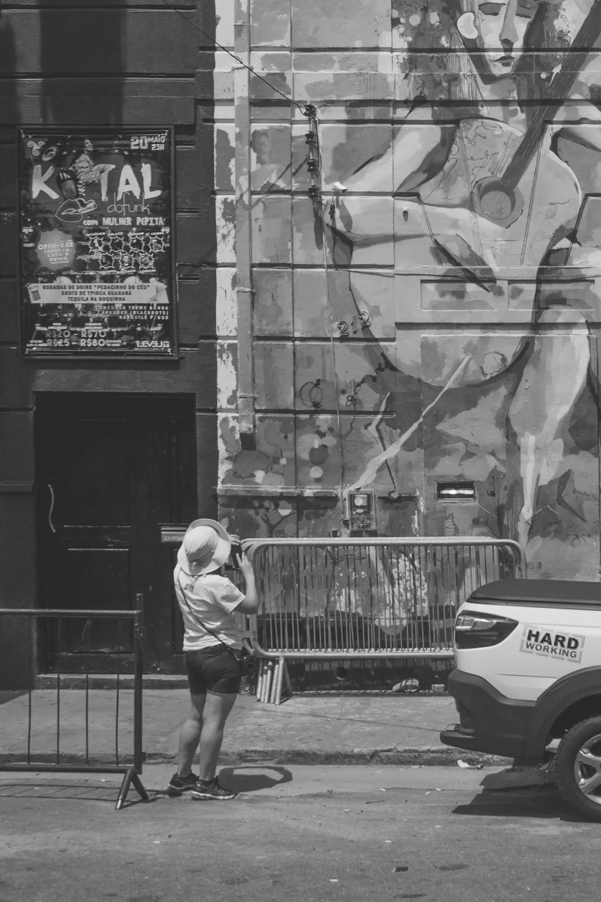 Fotografia em tons de cinza de um prédio antigo todo grafitado com uma mulher de costas segurando o celular enquanto fotografa o mural