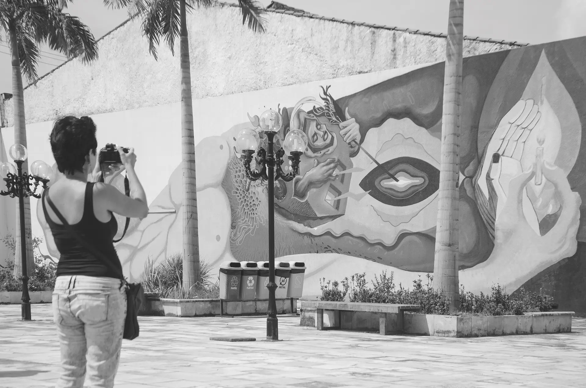 Fotografia em tons de cinza de uma mulher de costas fotografando um mural de graffiti no muro de uma praça no Centro de Fortaleza com uma câmera profissional